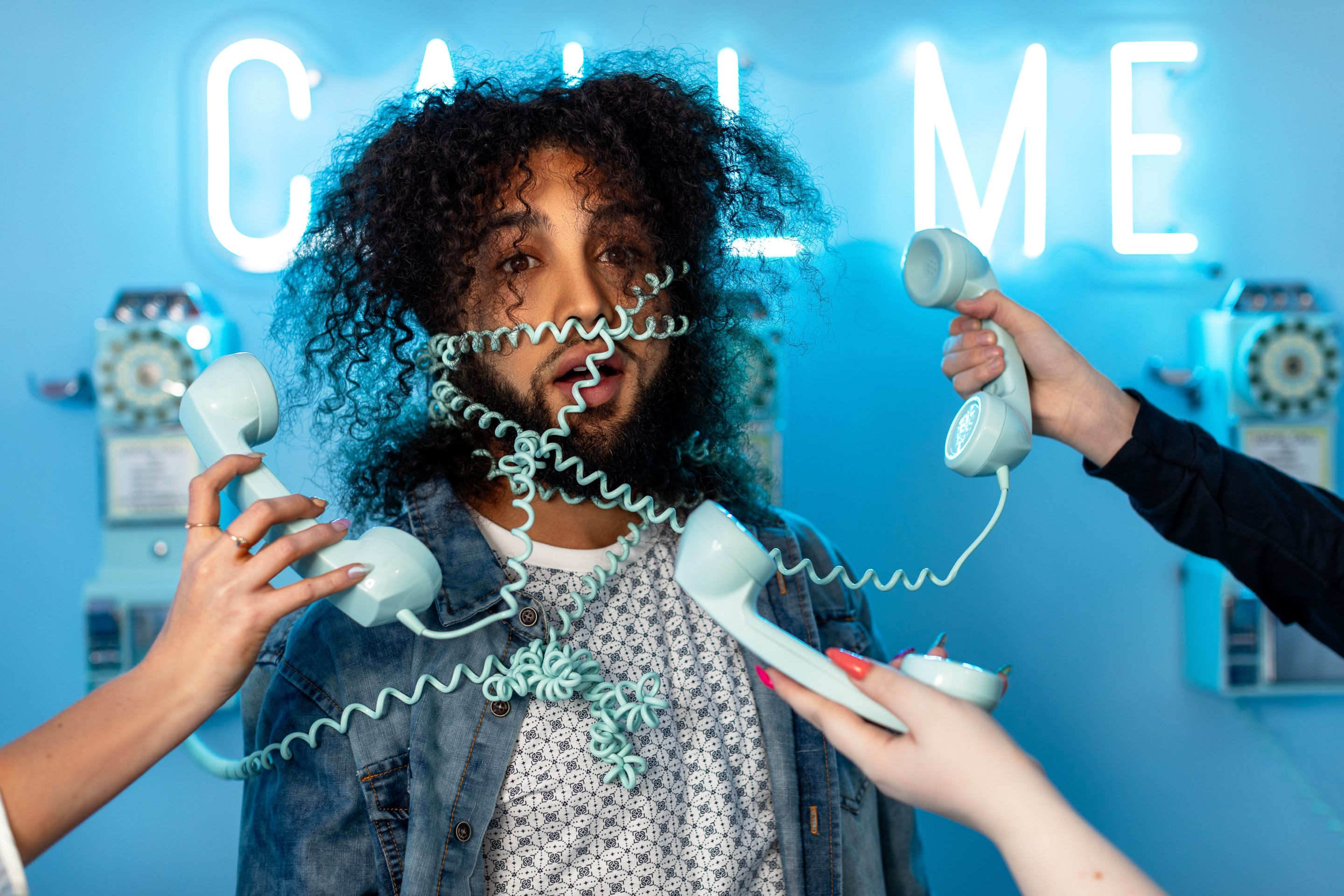 How to consistently hit sales quota Man wrapped around with phone cords, with a blue background and a neon sign that says "call me"