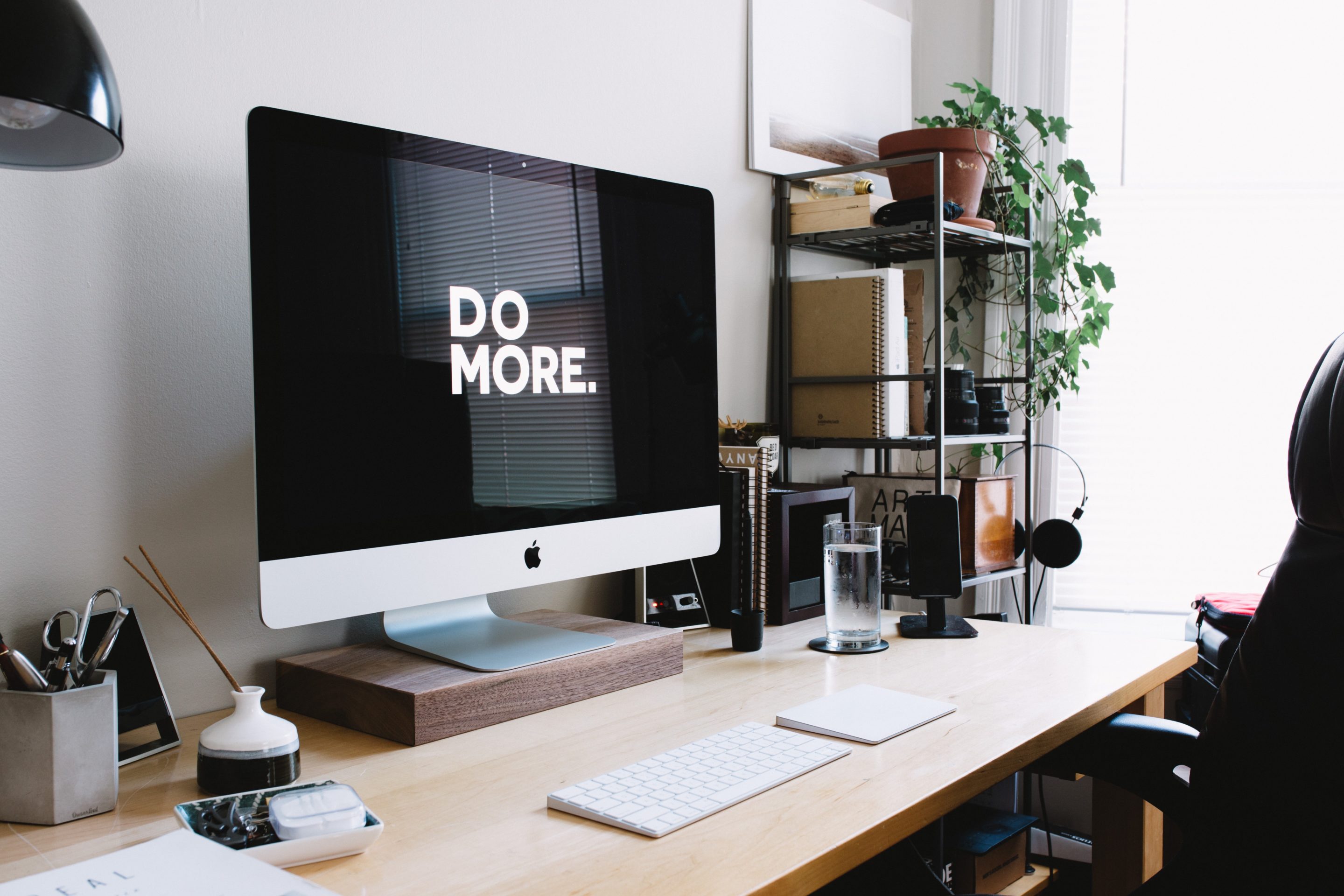 Home office desk with a Macbook computer on top that display the text "do more" in white with a black background