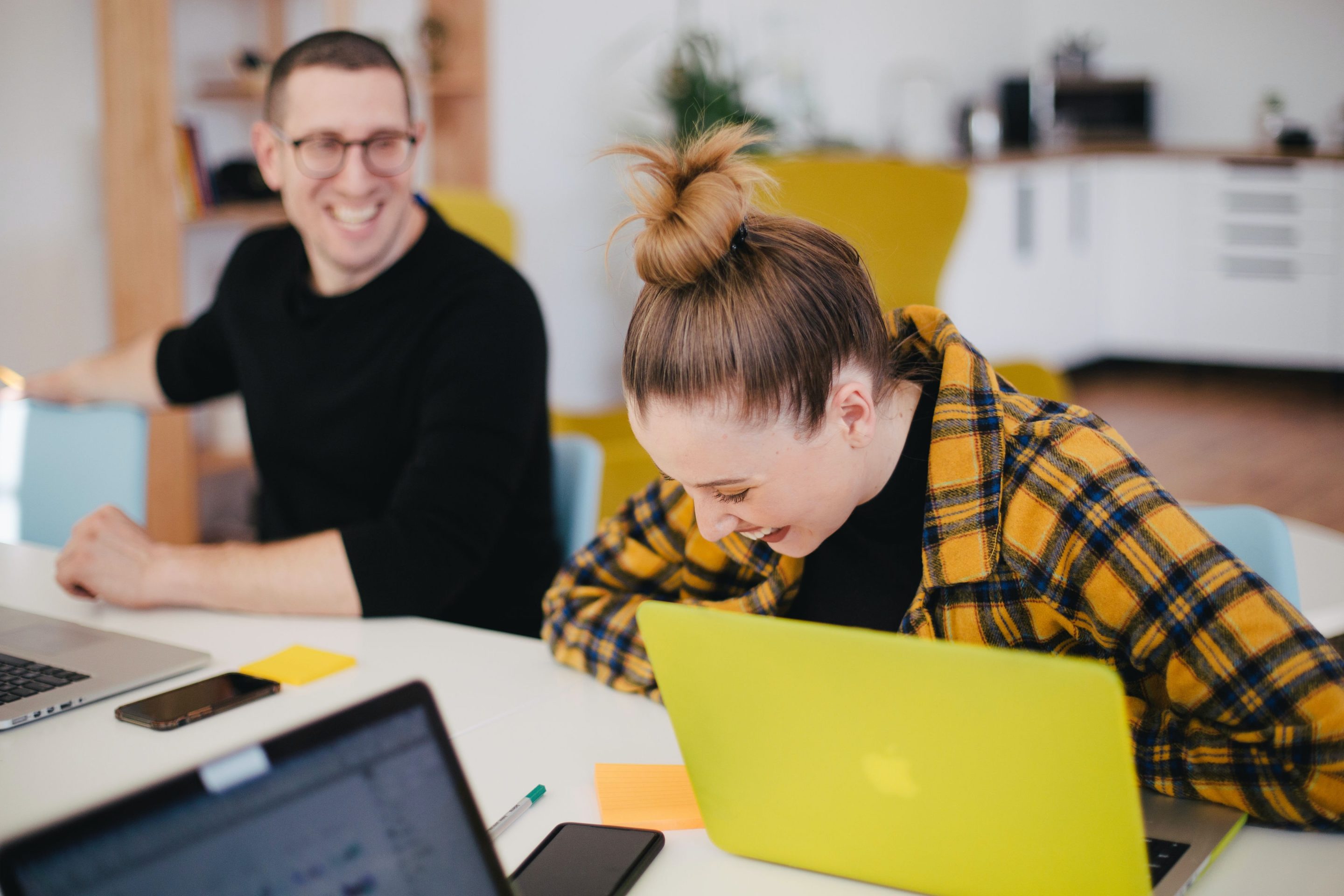 Selling doesn't have to be boring A man and a woman sitting in a desk with laptops laughing